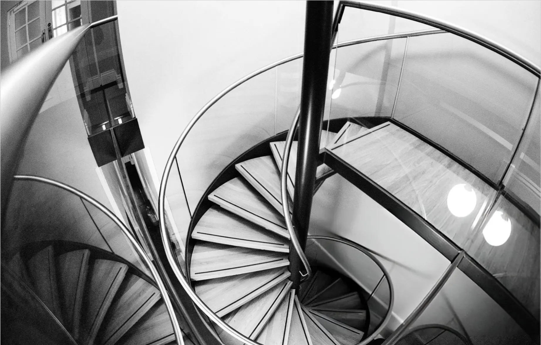 Stainless steel and glass spiral staircase photographed from above in black and white