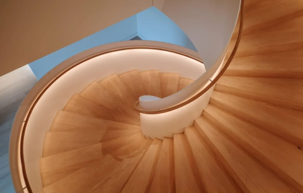 Helical timber staircase seen from above, with curved oak treads and a handrail lit by concealed strip lighting