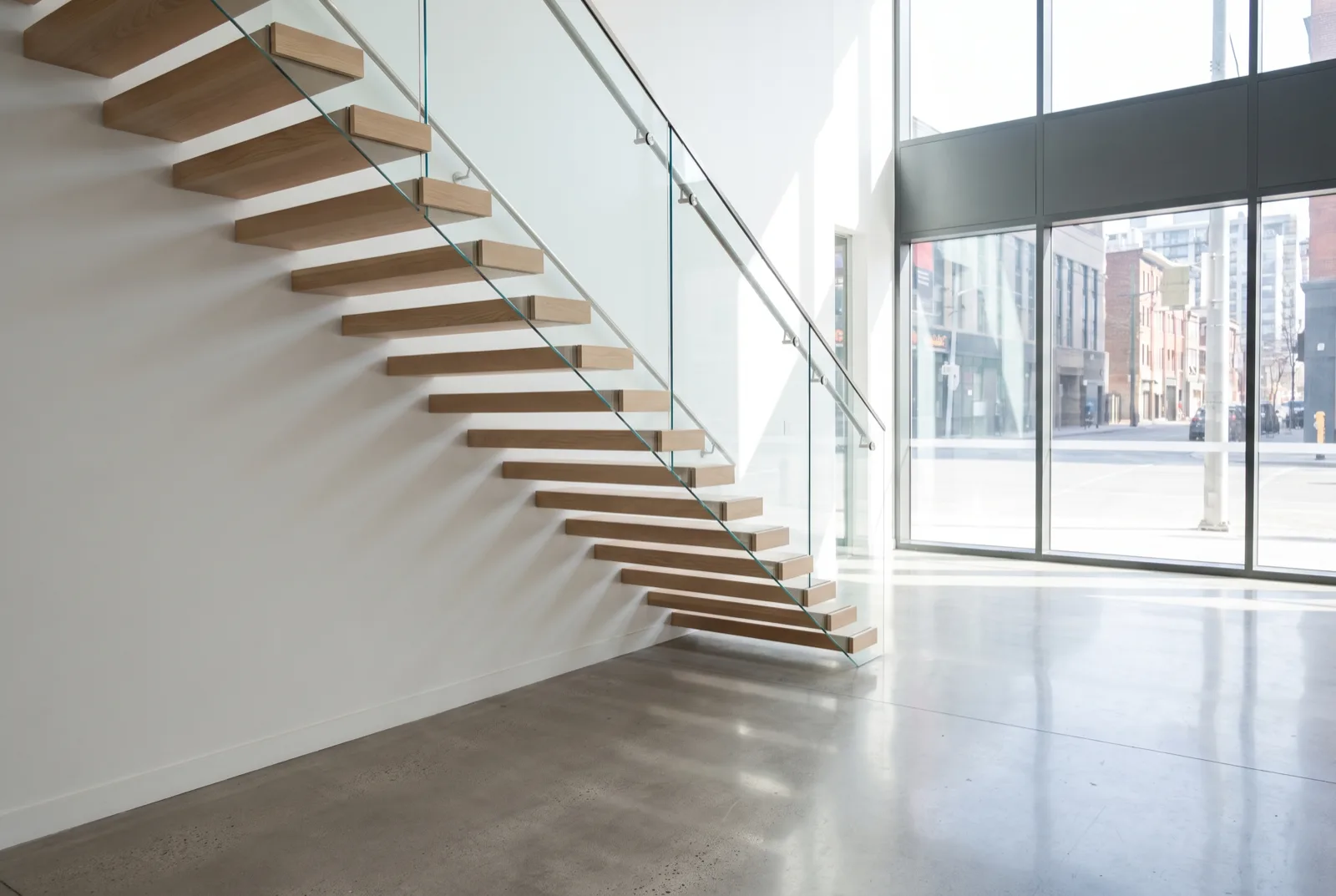 Straight cantilevered staircase with pale oak treads and a frameless glass balustrade in an office reception