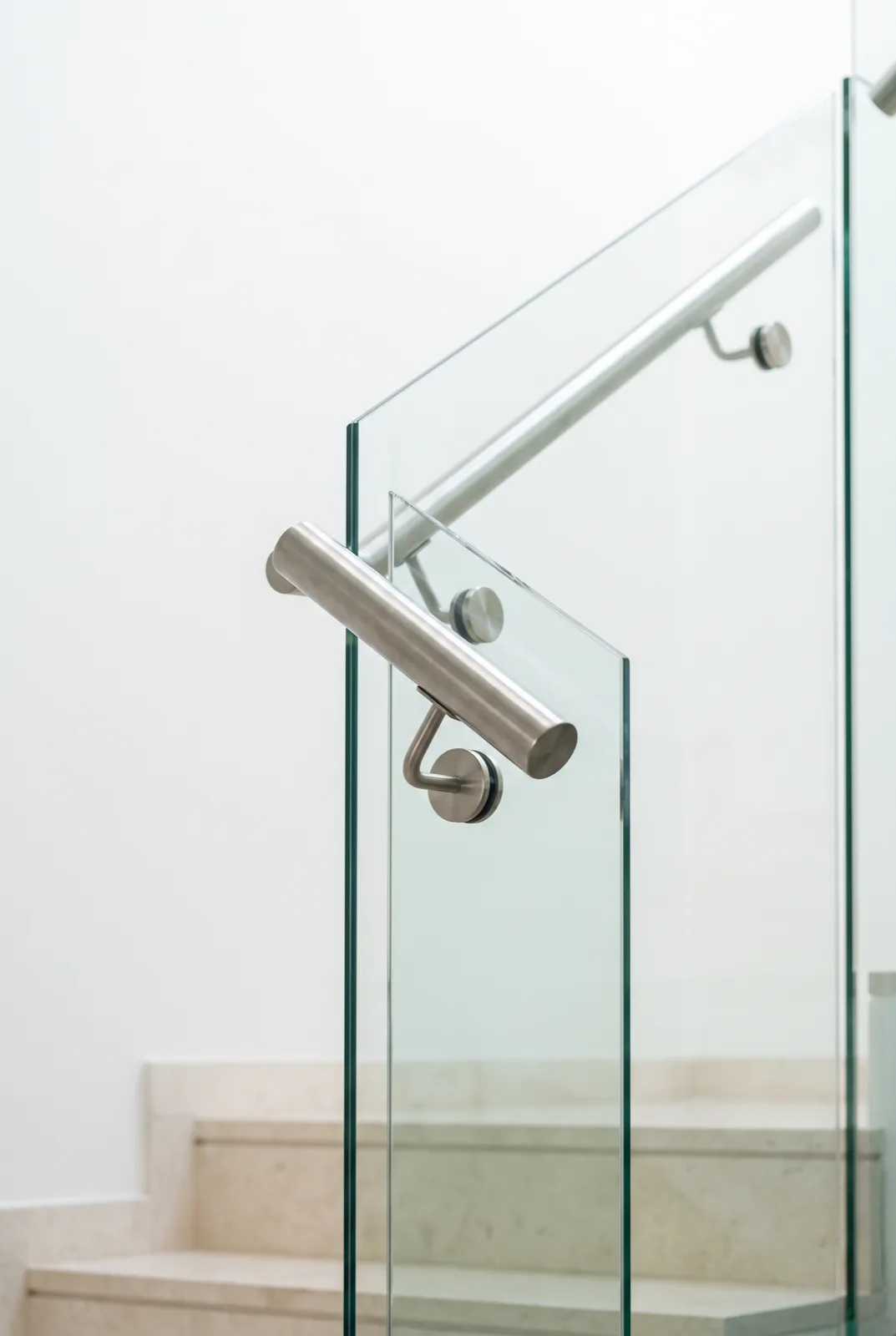 Close detail of a frameless glass staircase balustrade with a brushed stainless steel handrail and round standoff fittings